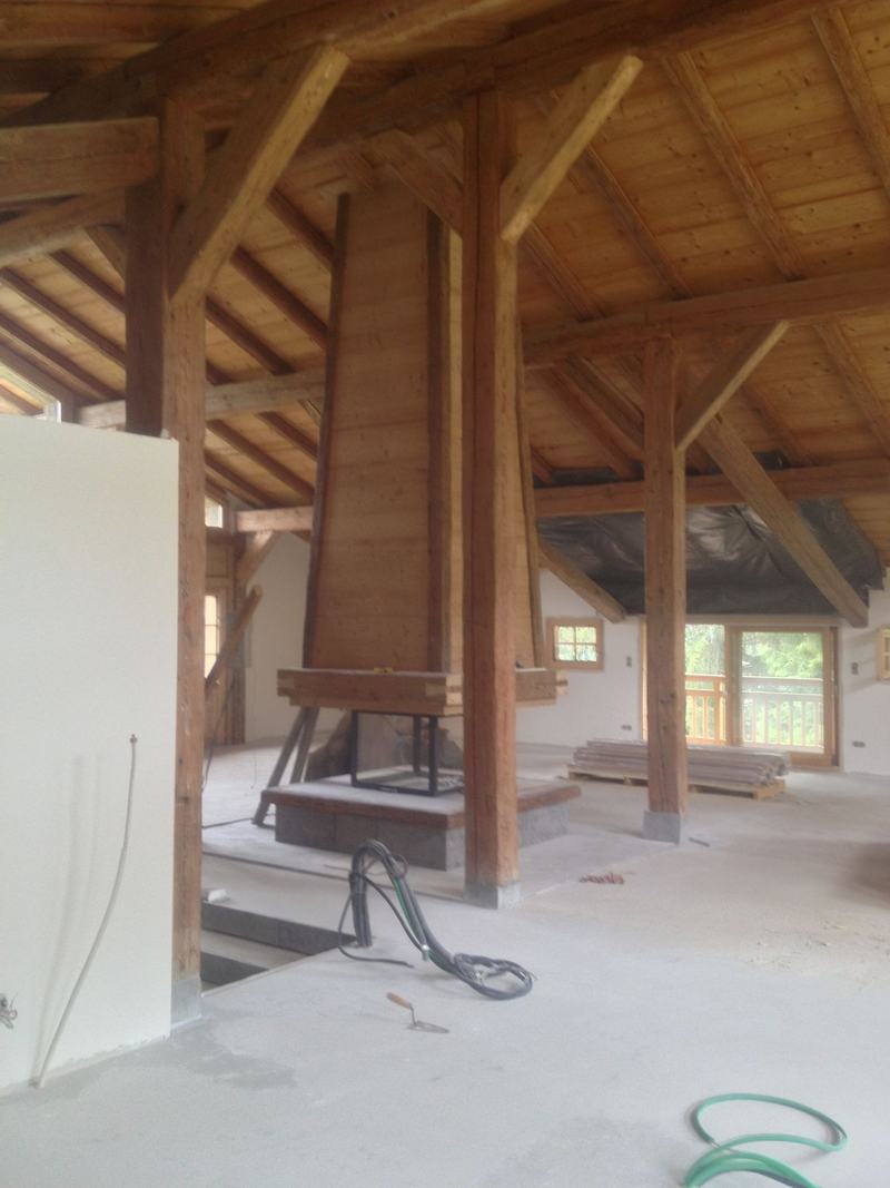 Grand volume de chalet sous charpente, poutres anciennes et cheminée habillée de bois